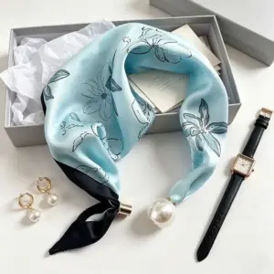 Hellblaues Tuch mit Blumenmuster und Perle am Knoten auf einer weißen Unterlage